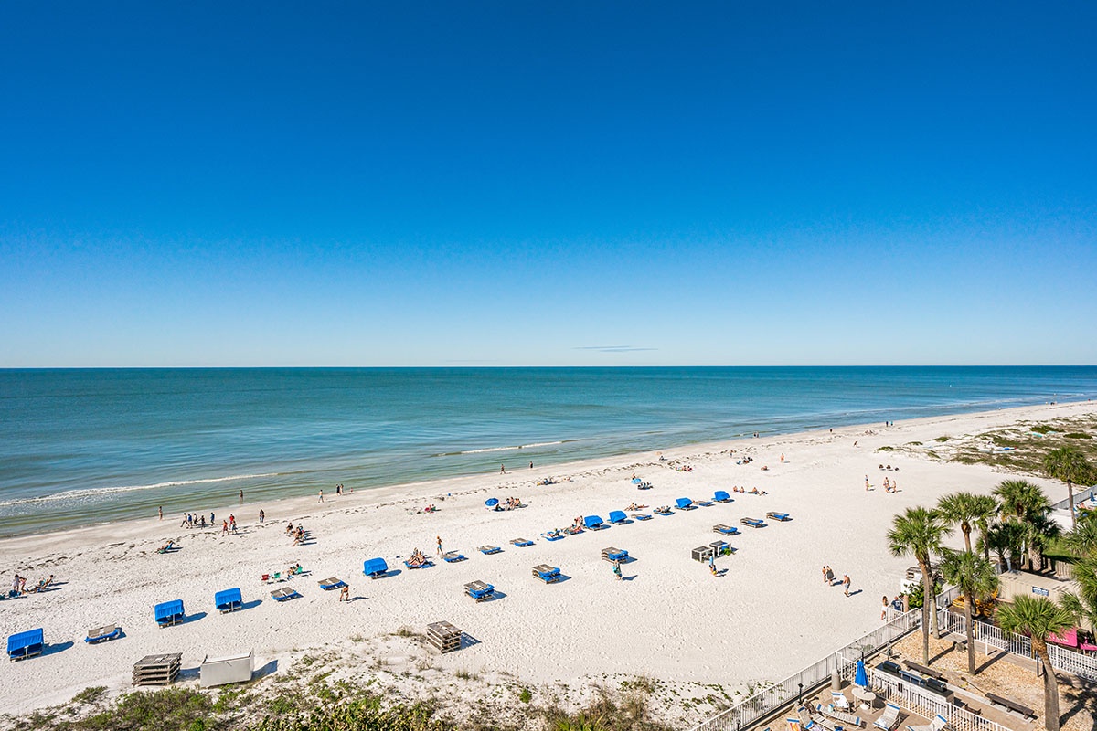 Pristine white sand beach stretches along crystal-clear waters under brilliant blue skies, offering an idyllic coastal retreat.