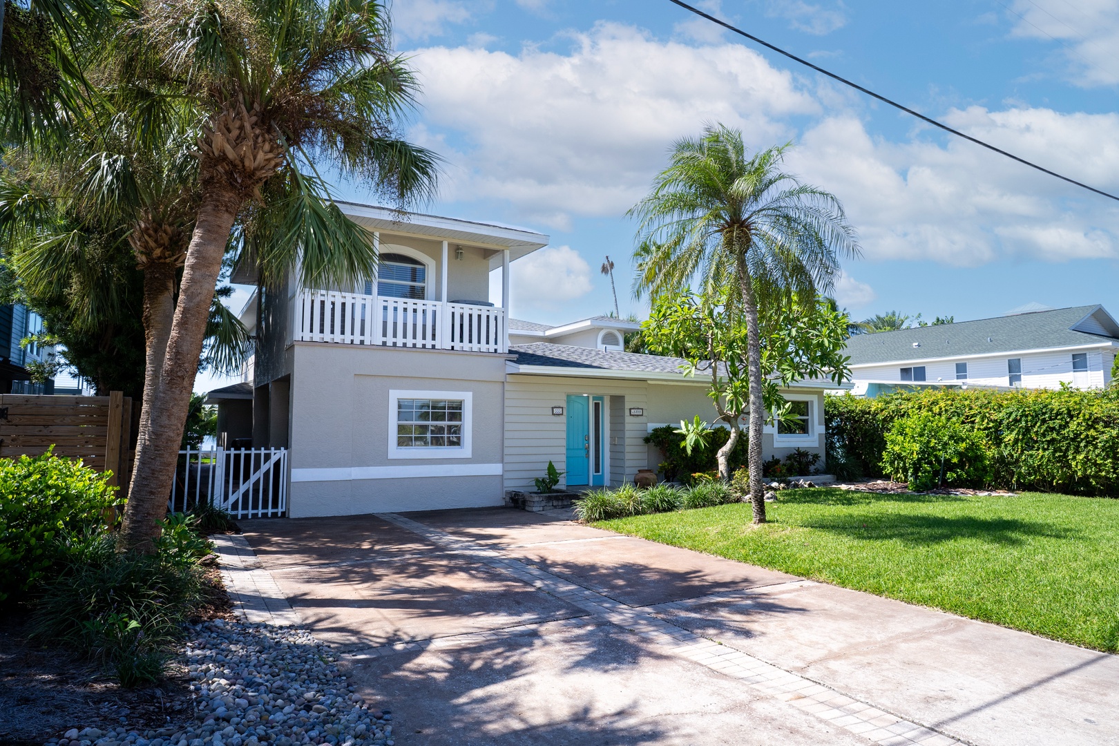 Charming coastal property featuring tropical landscaping with palm trees, bright blue door, and spacious driveway in a peaceful neighborhood setting.