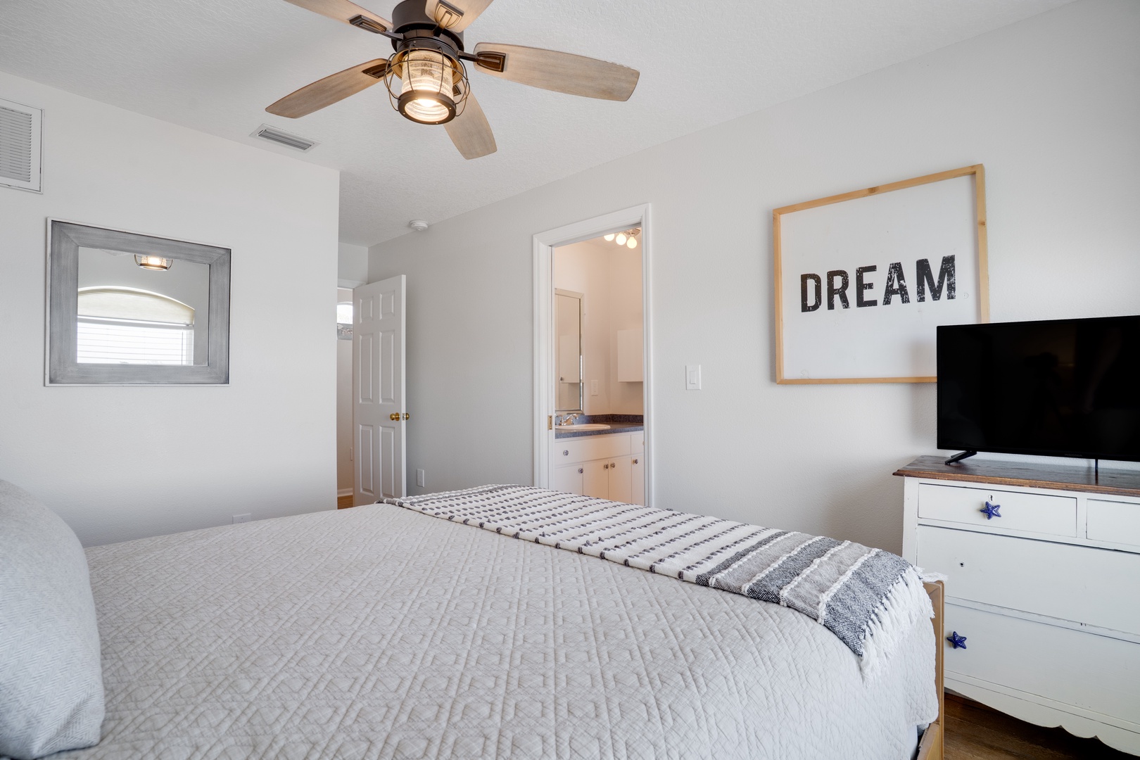 Drift off in your serene bedroom with crisp linens, ceiling fan, and inspiring artwork creating the perfect retreat.