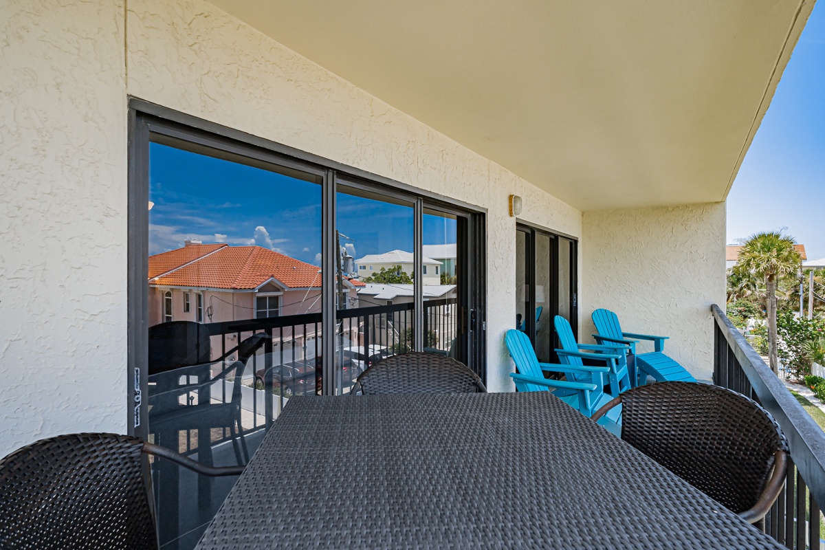 Spacious balcony with bright blue chairs and dining setup overlooks rooftops and palms, offering a sunny spot to relax, dine, or enjoy morning coffee in the coastal breeze.