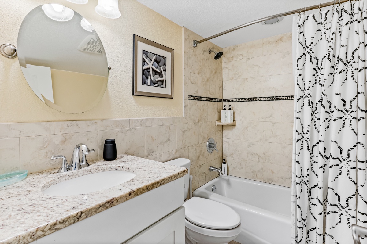 Refresh in your elegant marble bathroom featuring a granite vanity, stylish tile work, and convenient tub-shower combination.