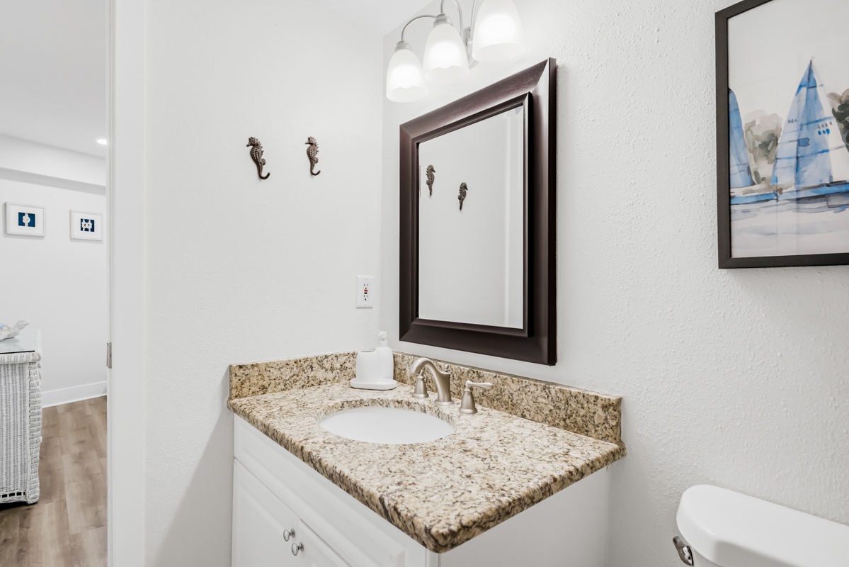 Refresh in your elegant bathroom featuring granite countertops, coastal artwork, and bright vanity lighting for your morning routine.