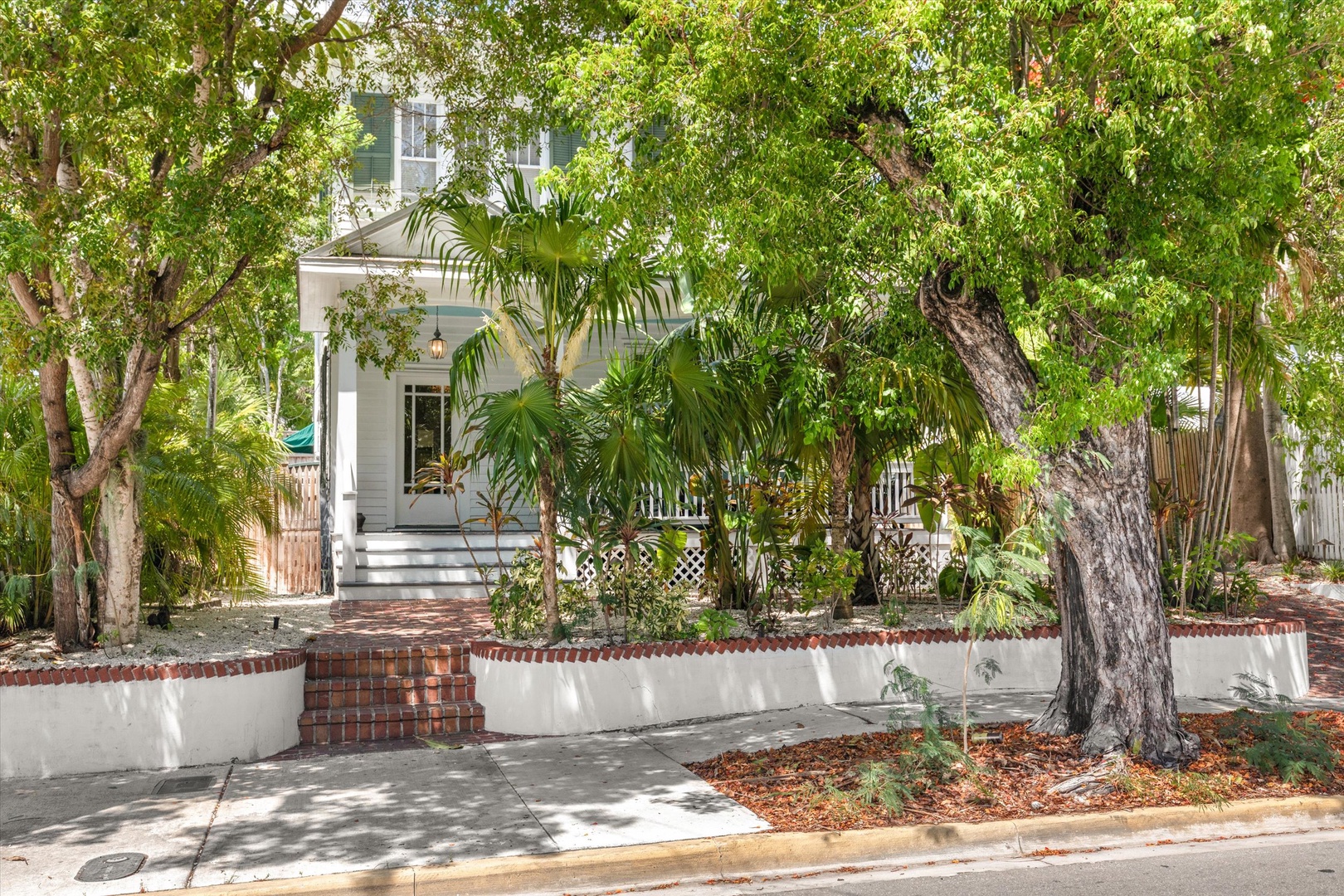 Charming two-story vacation home nestled in lush tropical greenery with welcoming front entrance, brick walkway, and abundant shade trees creating a private, peaceful retreat.