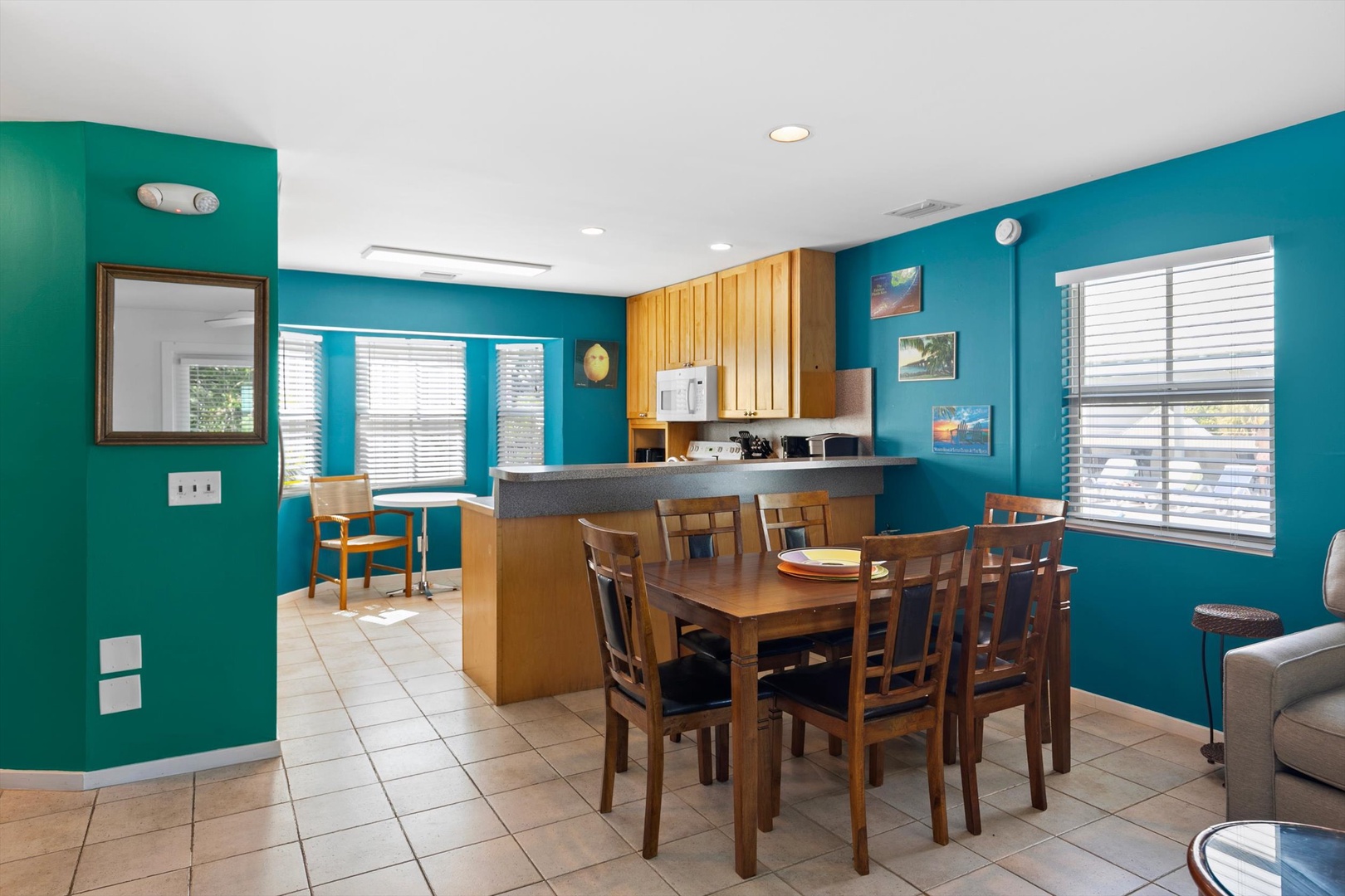 Gather around the dining table in this bright, open-plan space where vibrant turquoise walls meet warm wood finishes. Natural light floods through plantation shutters, creating a cheerful backdrop for your meals and memories together.