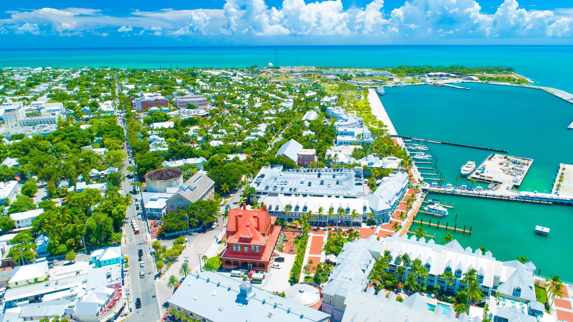 Aerial view of a vibrant coastal town with a marina, historic buildings, and lush tropical vegetation surrounded by turquoise waters.
