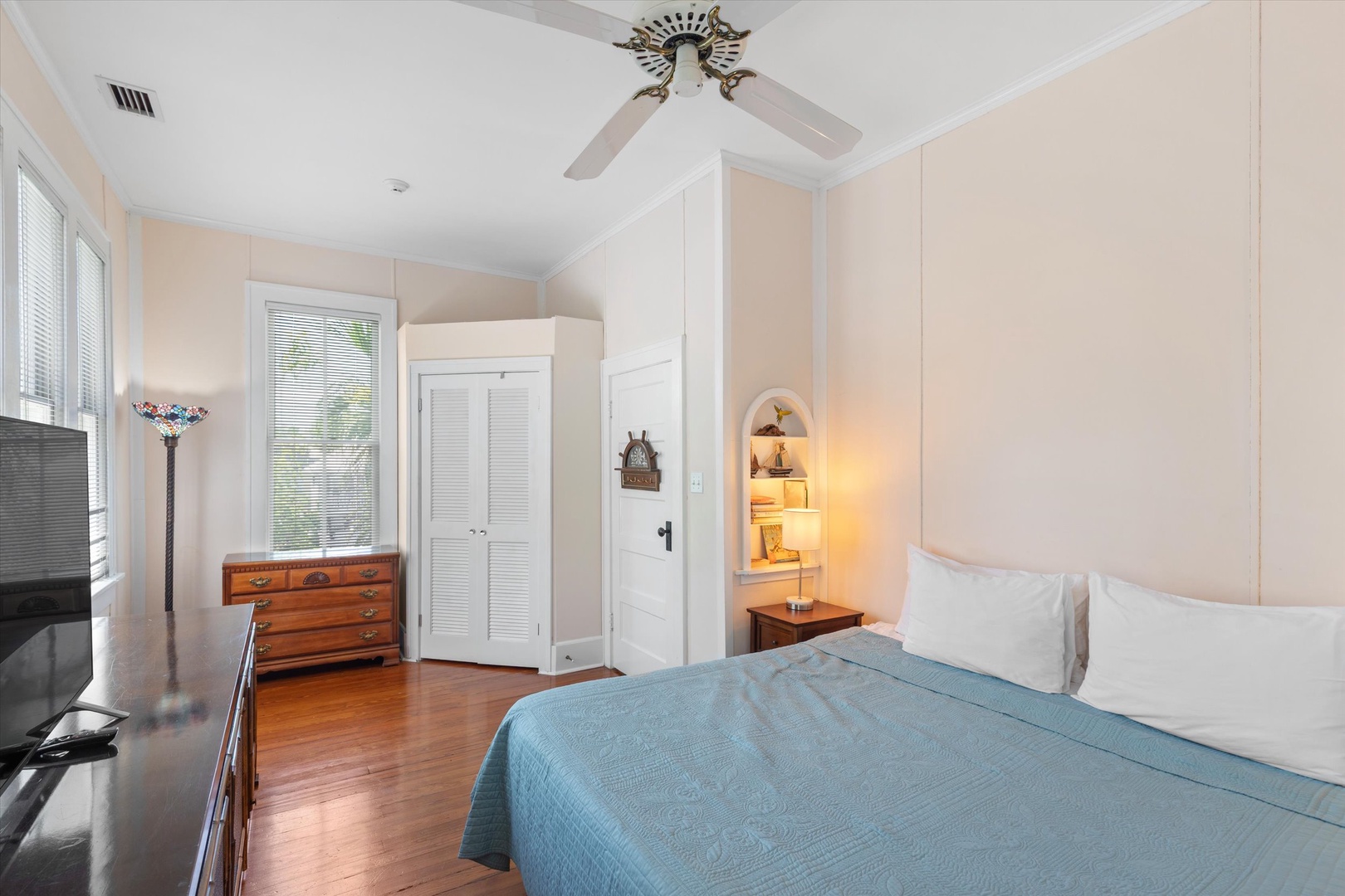 Unwind in your serene bedroom with elegant wood floors, gentle ceiling fan breeze, and soft coastal touches that invite peaceful rest after a day exploring.