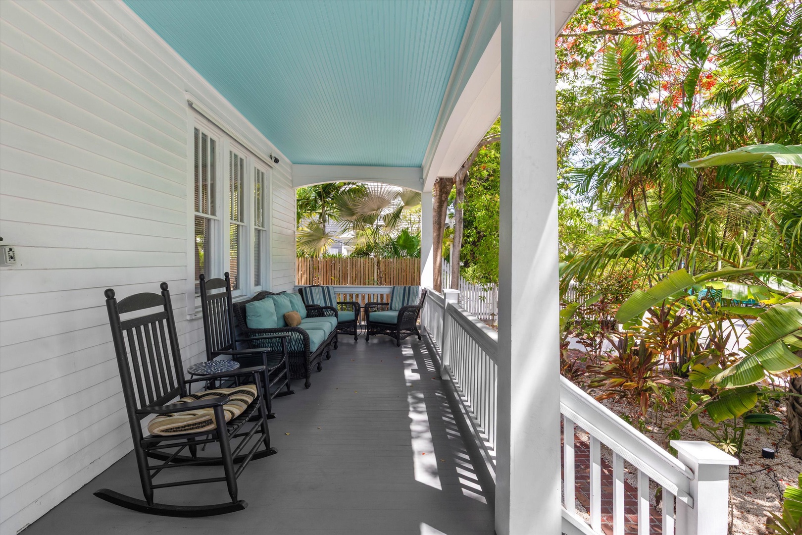Sip your morning coffee on this covered porch, where rocking chairs and cushioned seating invite you to unwind amid tropical greenery and gentle breezes.