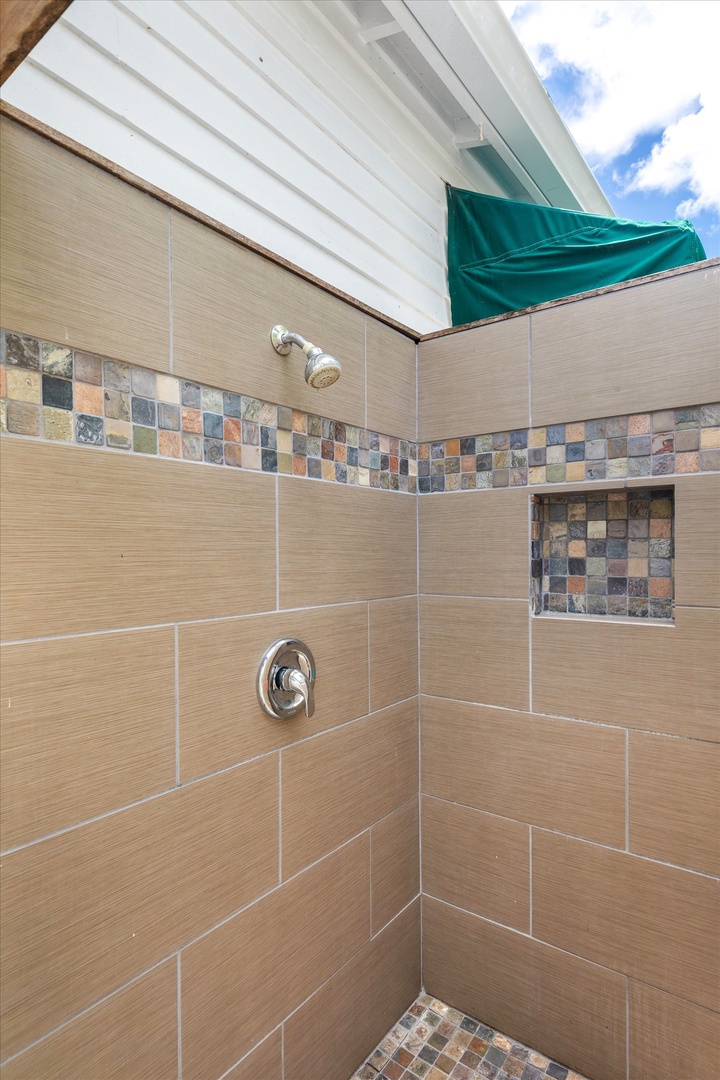 Modern outdoor shower features warm beige tile with colorful mosaic accents, blending style and function for post-beach rinses under open skies.