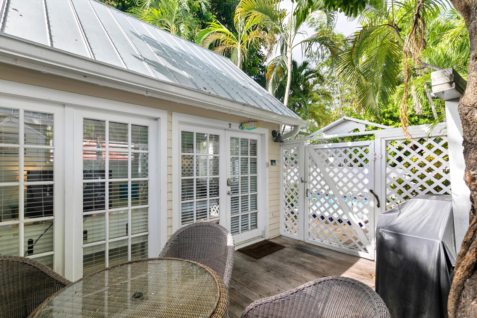 Your private deck invites you to relax under swaying palms, with wicker seating and tropical greenery just beyond the lattice gate.