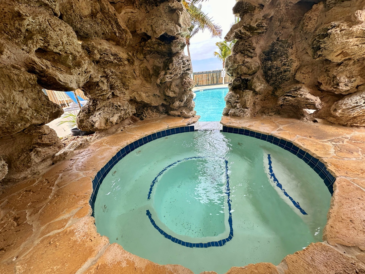Imagine yourself soaking in this stunning grotto-style hot tub, surrounded by natural rock formations with a view of the sparkling pool beyond.