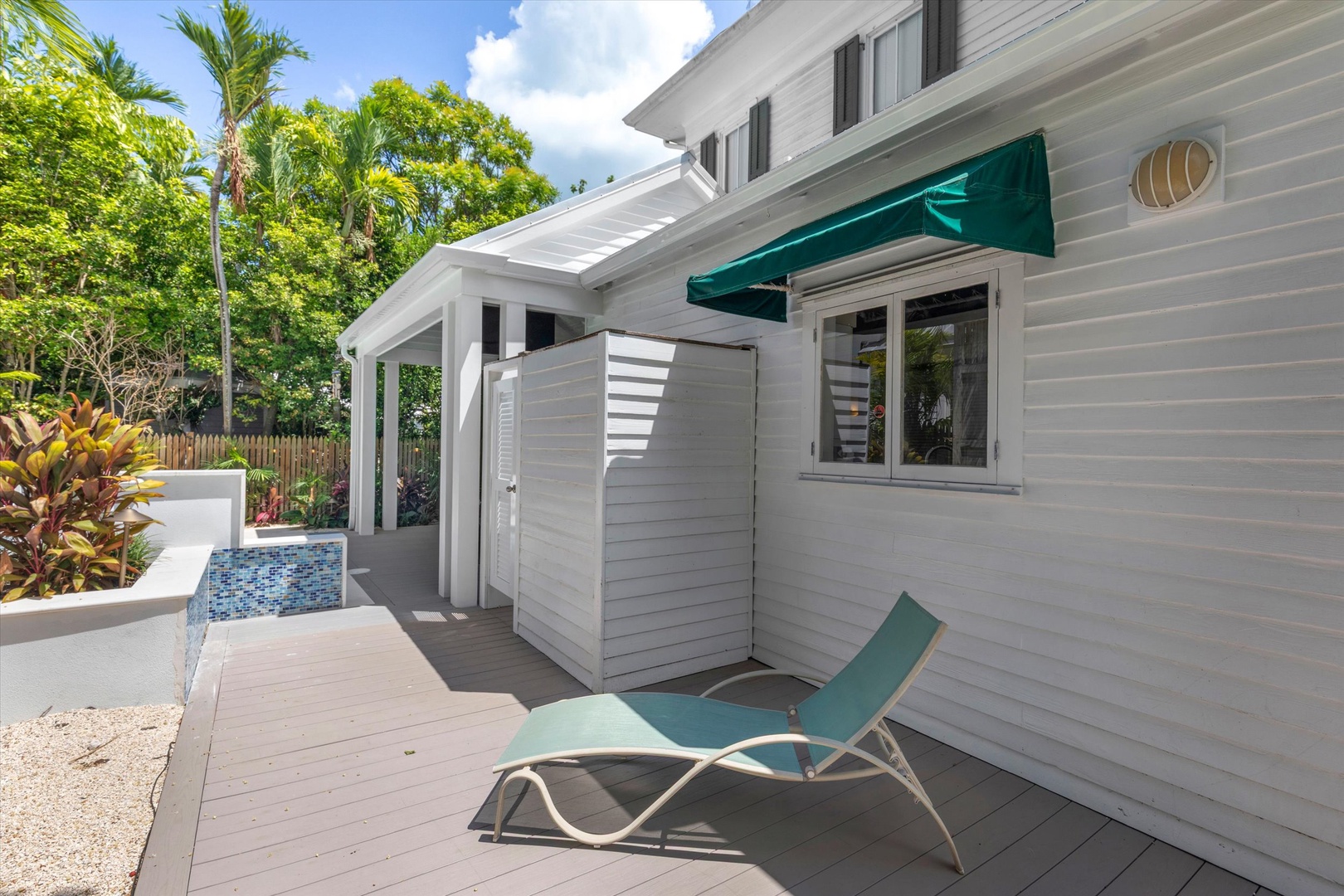 This charming white cottage features a private outdoor deck with a lounger, surrounded by lush tropical landscaping and palm trees for peaceful relaxation.
