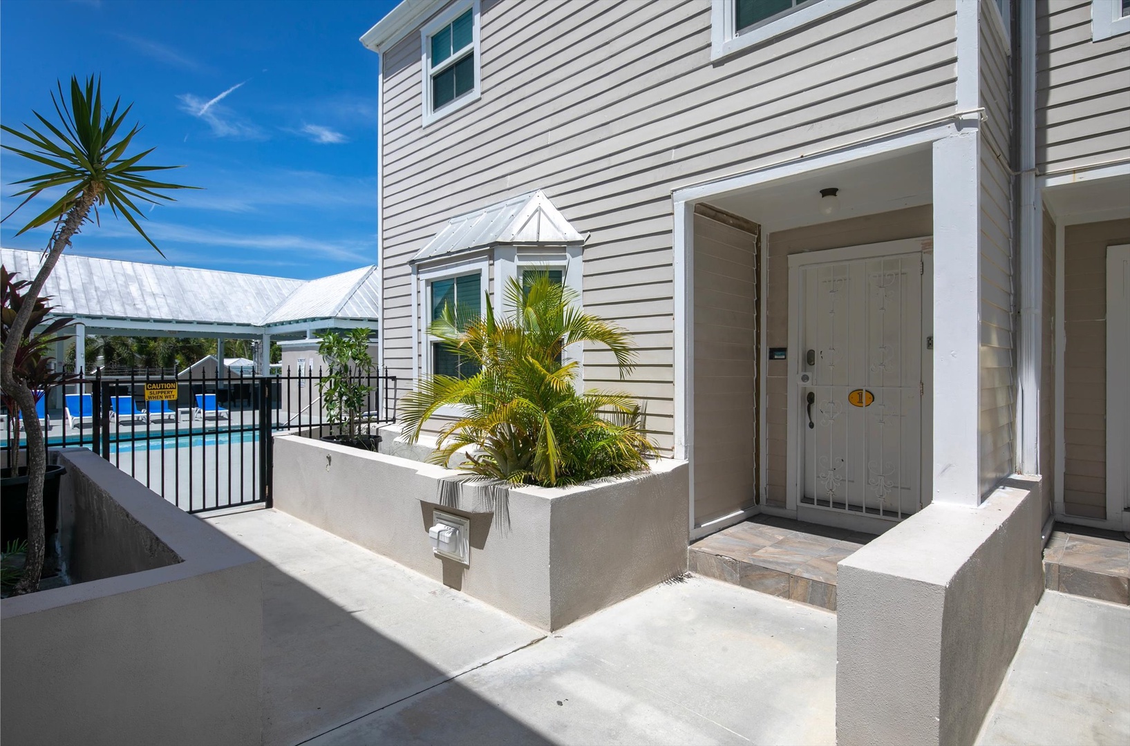 Welcome to a bright coastal retreat. Your private entrance opens to vibrant tropical landscaping, with lush palms greeting you at the door. A sparkling pool awaits just steps away for refreshing afternoons under sunny skies.