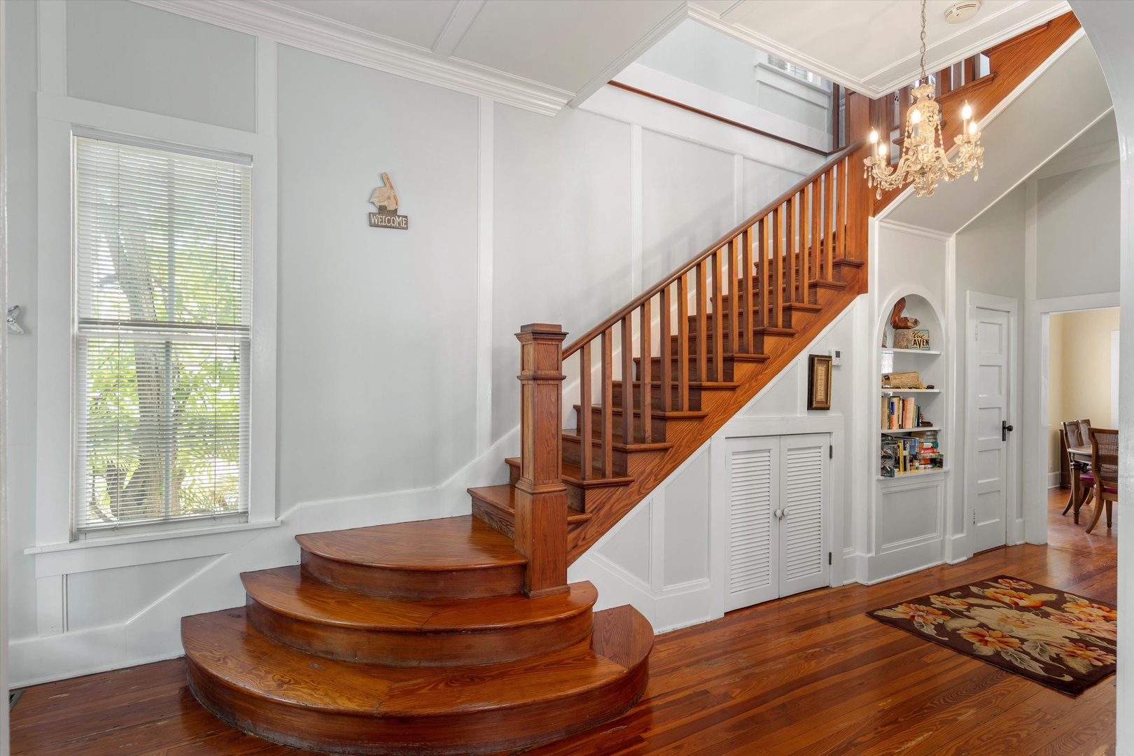Step into the elegant foyer where a stunning curved wooden staircase greets you. High ceilings, gleaming hardwood floors, and a sparkling chandelier create a warm, welcoming atmosphere perfect for your vacation retreat.