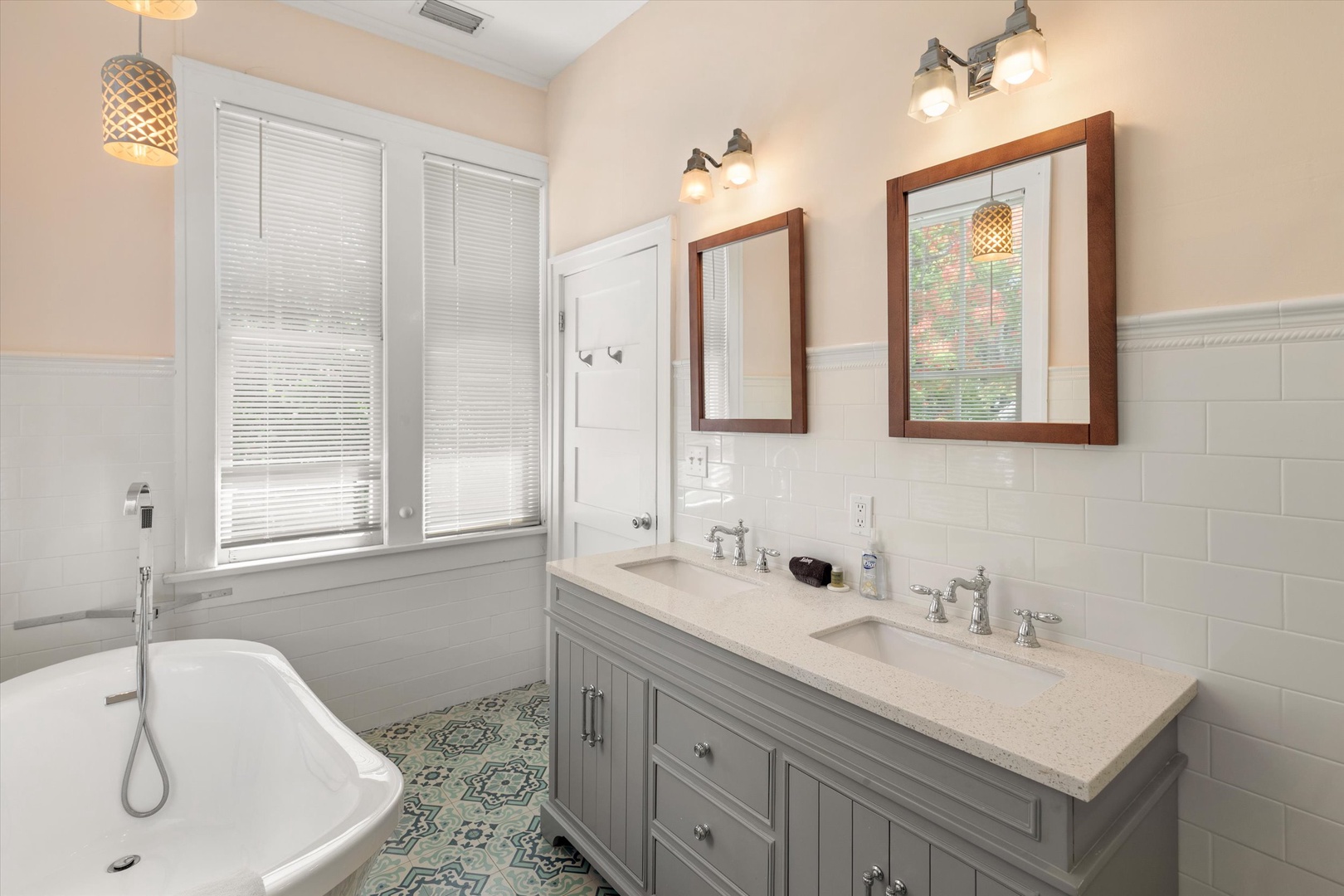 Unwind in your serene bathroom featuring a luxurious soaking tub, dual vanities, and natural light from large windows. The elegant tilework and warm lighting create a spa-like retreat for your stay.