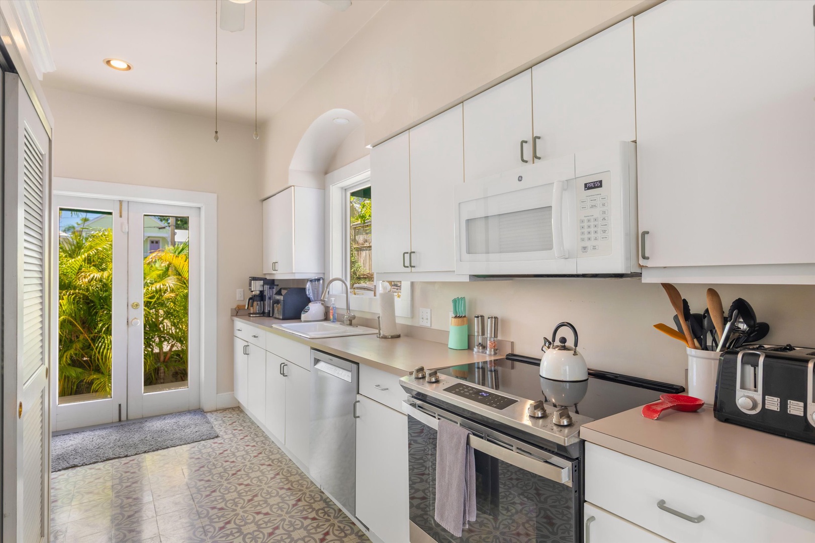 Cook up your vacation favorites in this bright, fully-equipped kitchen with modern appliances, ample counter space, and natural light streaming through French doors that open to lush tropical gardens.