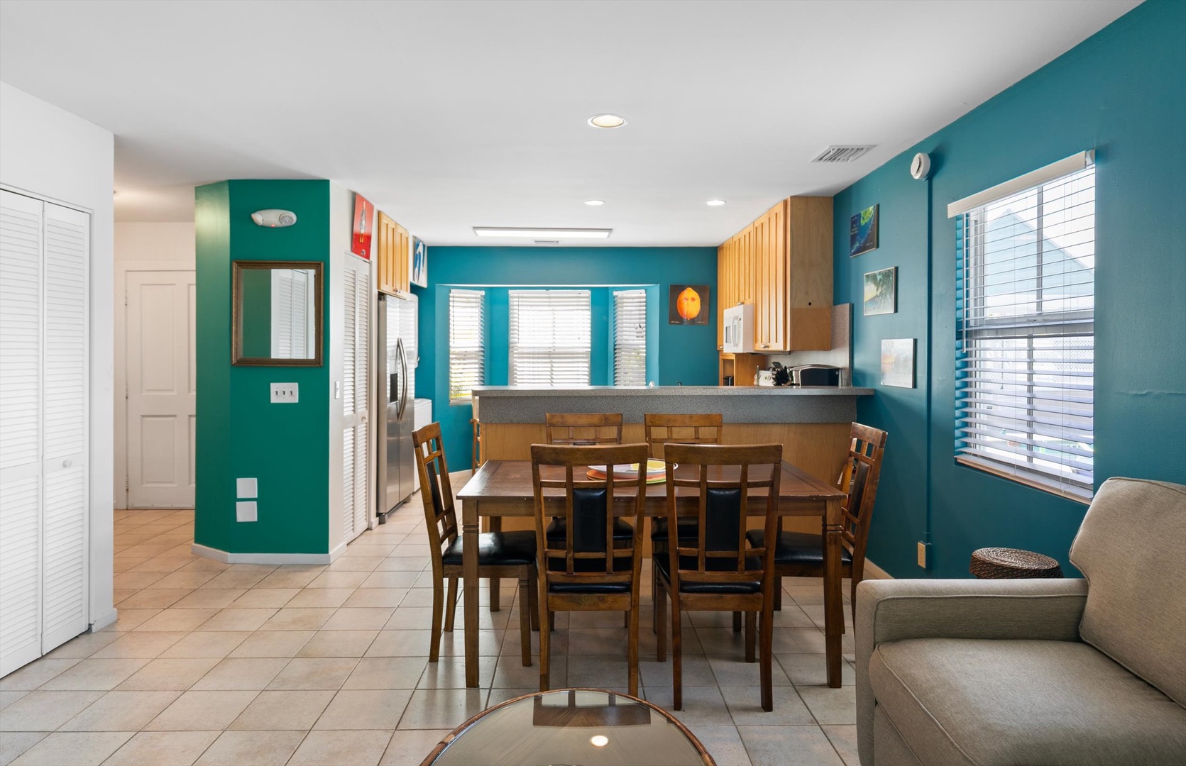 Gather around the large dining table in your bright, open-concept living space, framed by vibrant teal walls and flooded with natural light—perfect for group meals and laughter.