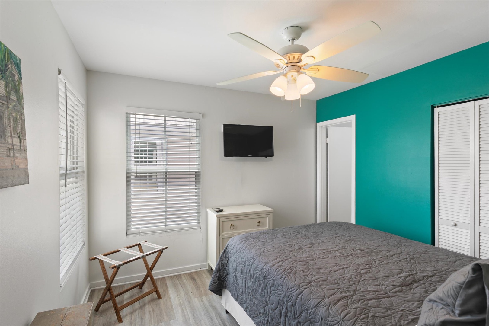 Bright and airy bedroom with vibrant teal accent wall, ceiling fan, and convenient TV—perfect for winding down after your adventures.