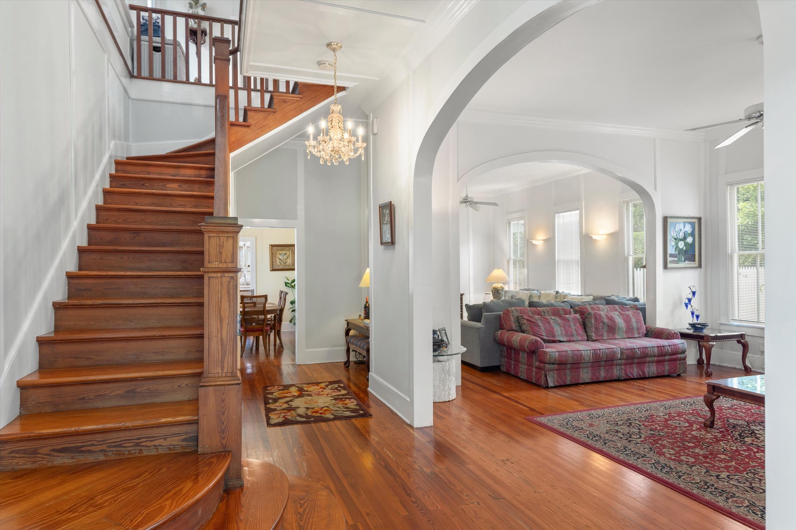 Step into elegance with gleaming hardwood floors, a graceful staircase, and grand archway leading to your inviting living space. The chandelier casts a warm glow throughout this charming home.