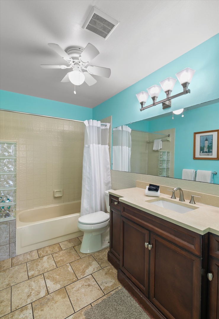 Your bright turquoise bathroom welcomes you with fresh white towels, a ceiling fan for comfort, and a tub-shower combo perfect for unwinding after beach adventures.