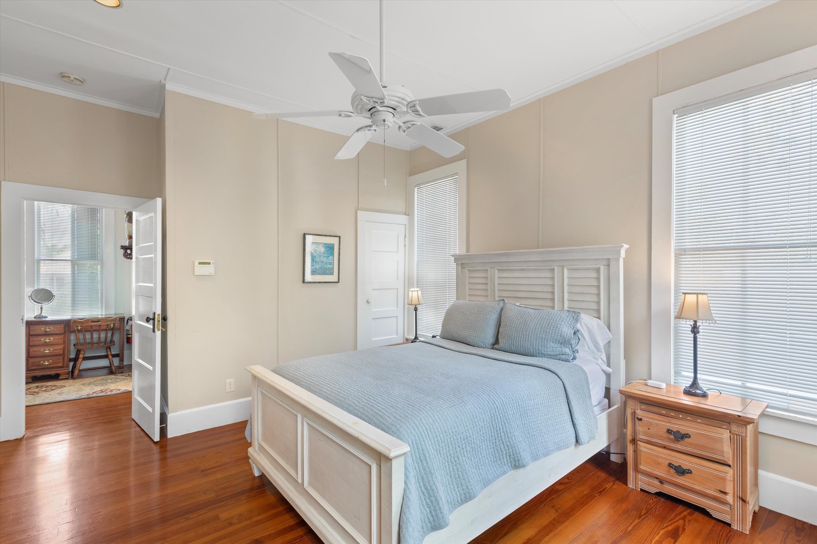 Relax in your peaceful bedroom with gleaming hardwood floors, soft blue linens, and natural light streaming through large windows to brighten your stay.