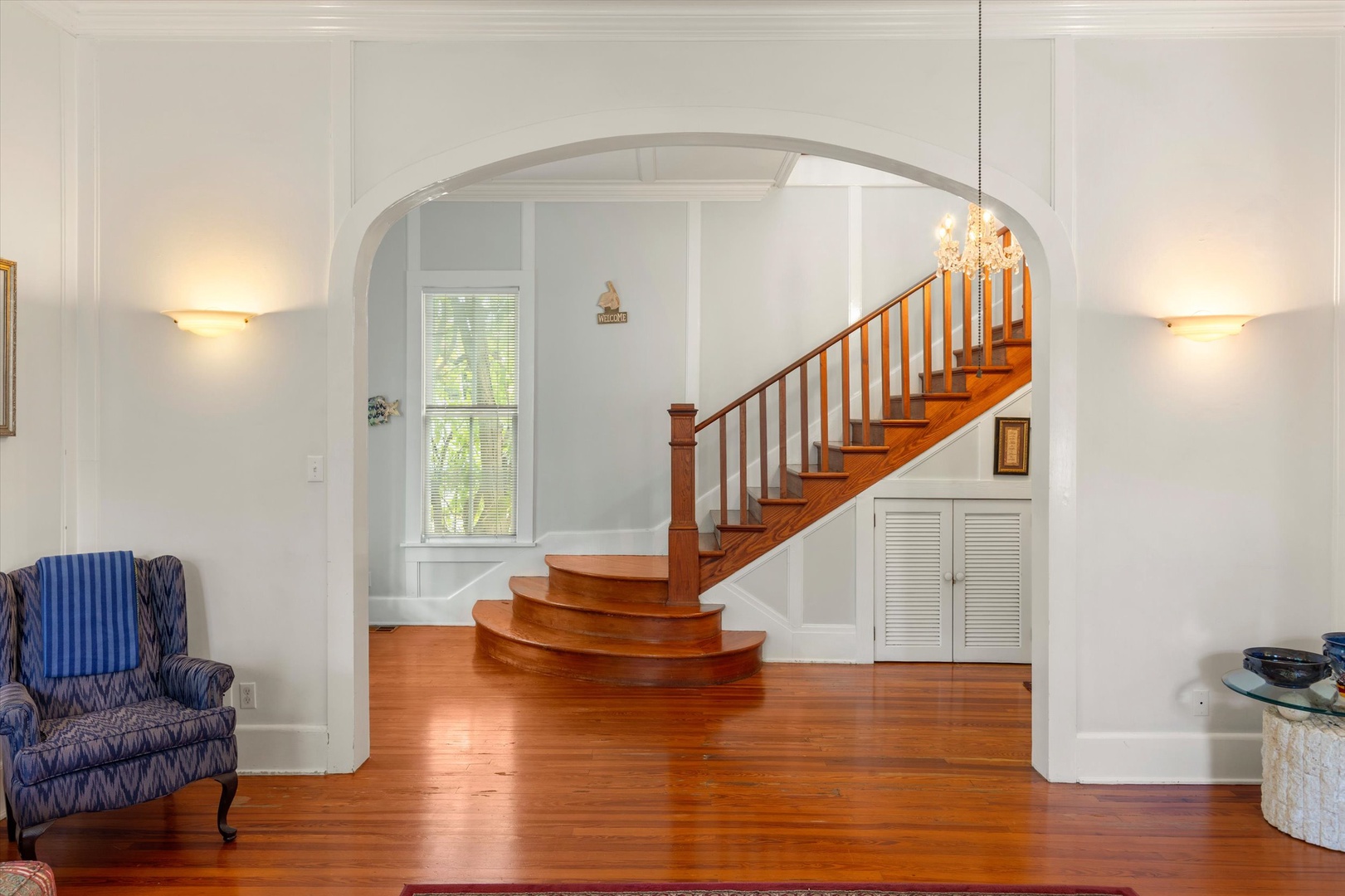 Step into a bright, welcoming foyer where warm wooden floors and an elegant curved staircase create a graceful first impression for your arrival.