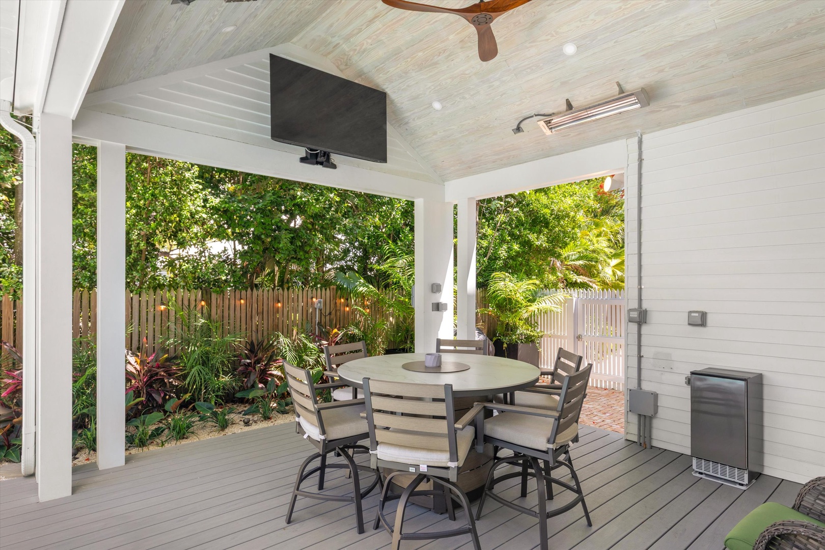 Gather around the outdoor dining table on your private covered patio, surrounded by lush tropical greenery and equipped with ceiling fan and TV for perfect alfresco entertaining.