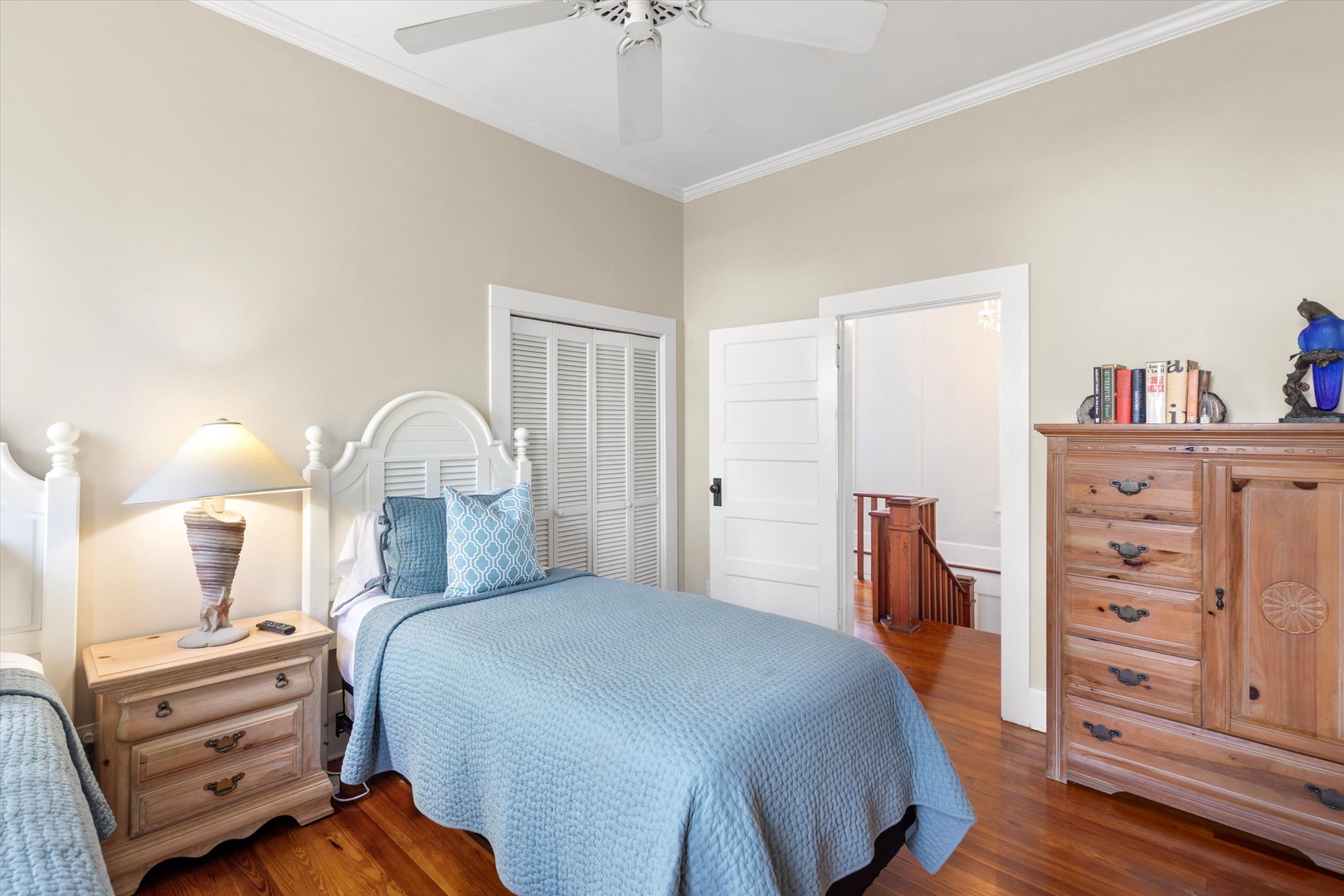 Cozy bedroom with warm hardwood floors, soft blue linens, and classic furnishings. A ceiling fan keeps you comfortable while antique-style pieces add charming character to your restful retreat.