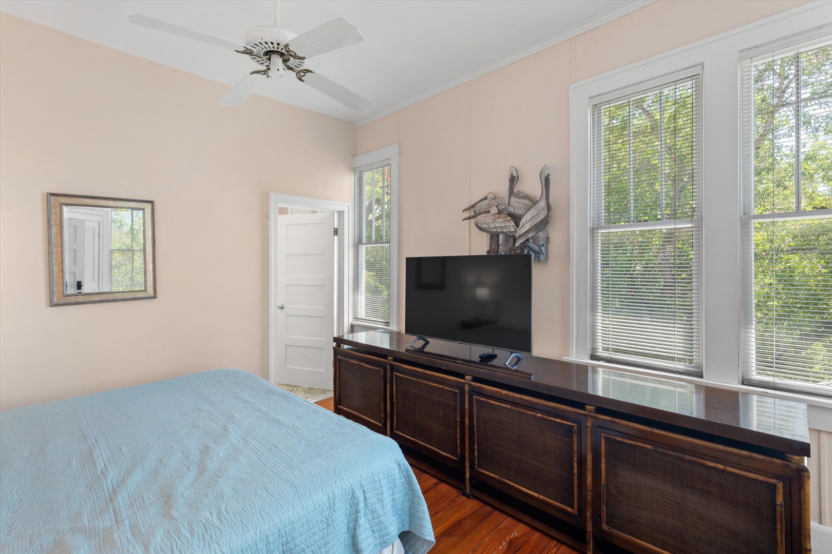 Relax in this peaceful bedroom where natural light filters through large windows, highlighting polished wood floors and a cozy bed. Enjoy your favorite shows on the flat-screen TV after a day of adventure.