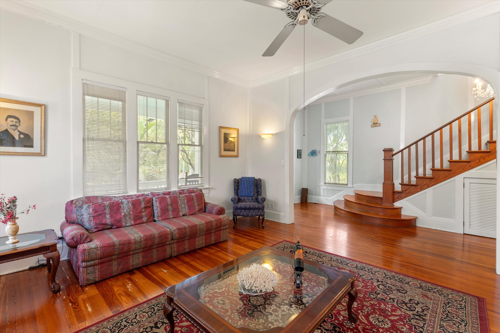 Step into a bright, airy living room where polished hardwood floors gleam beneath your feet and soaring ceilings invite relaxation. Curl up on comfortable seating, let the ceiling fan keep you cool, and enjoy the warm natural light.