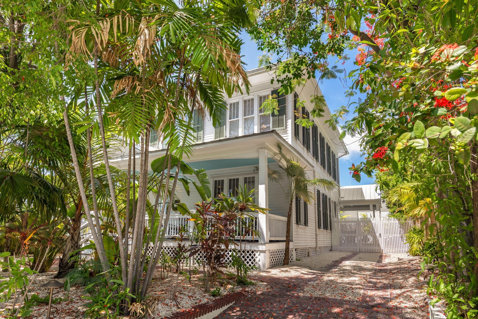 This charming two-story home sits nestled in lush tropical foliage, with vibrant palms and flowering plants framing its welcoming facade—a private island escape.