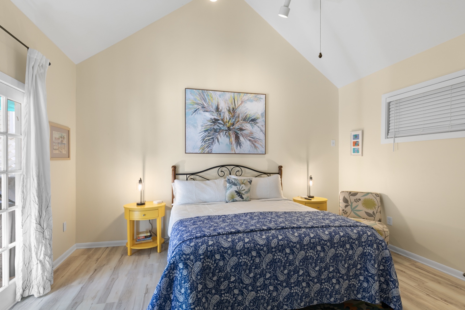 Slip into this airy bedroom with soaring ceilings and coastal charm. Your bed awaits beneath soft linens and island-inspired art, while cheerful pops of yellow brighten the space.