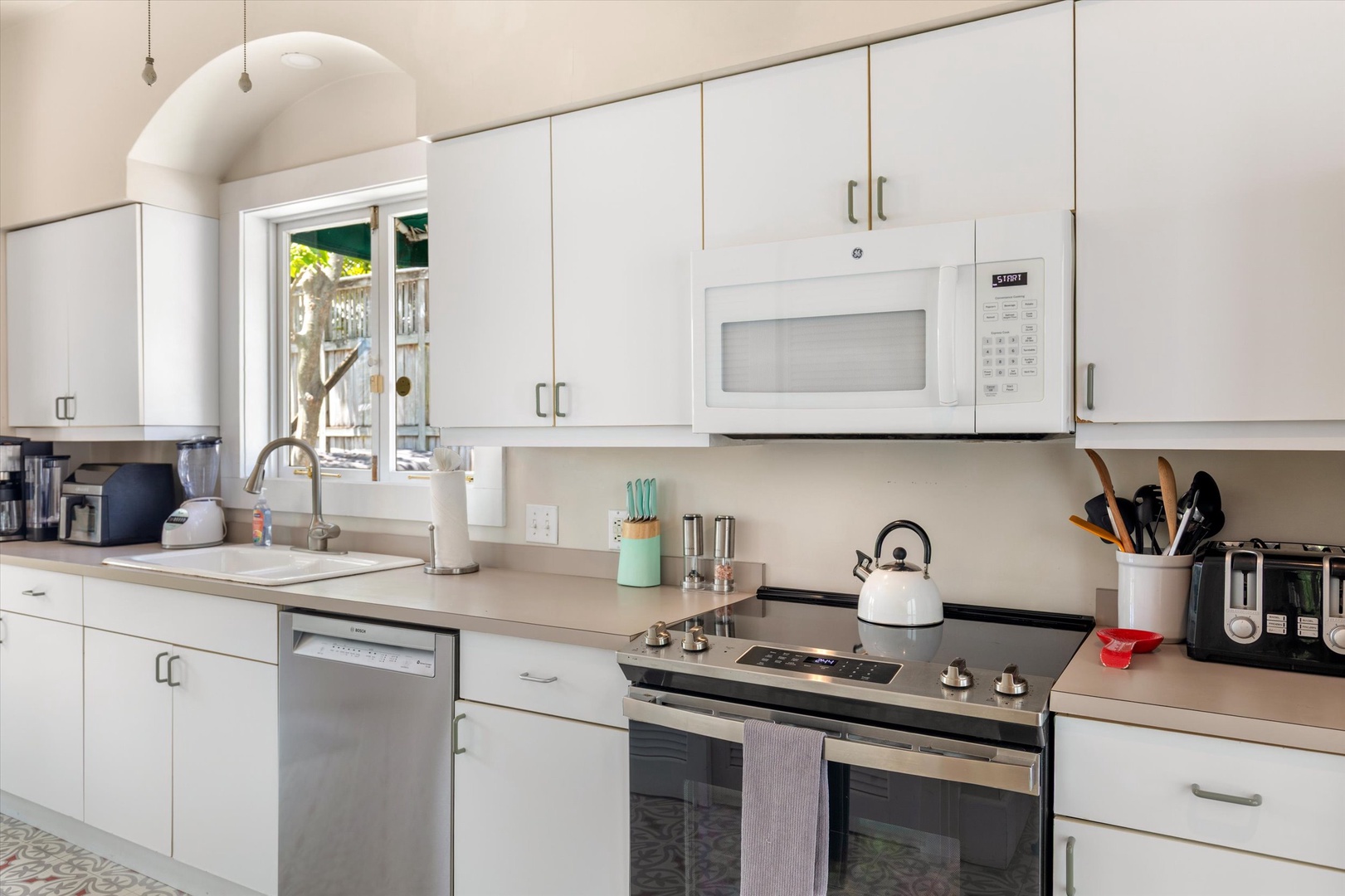 Prepare your favorite meals in this bright, fully-equipped kitchen with modern appliances, ample counter space, and natural light streaming through the window.