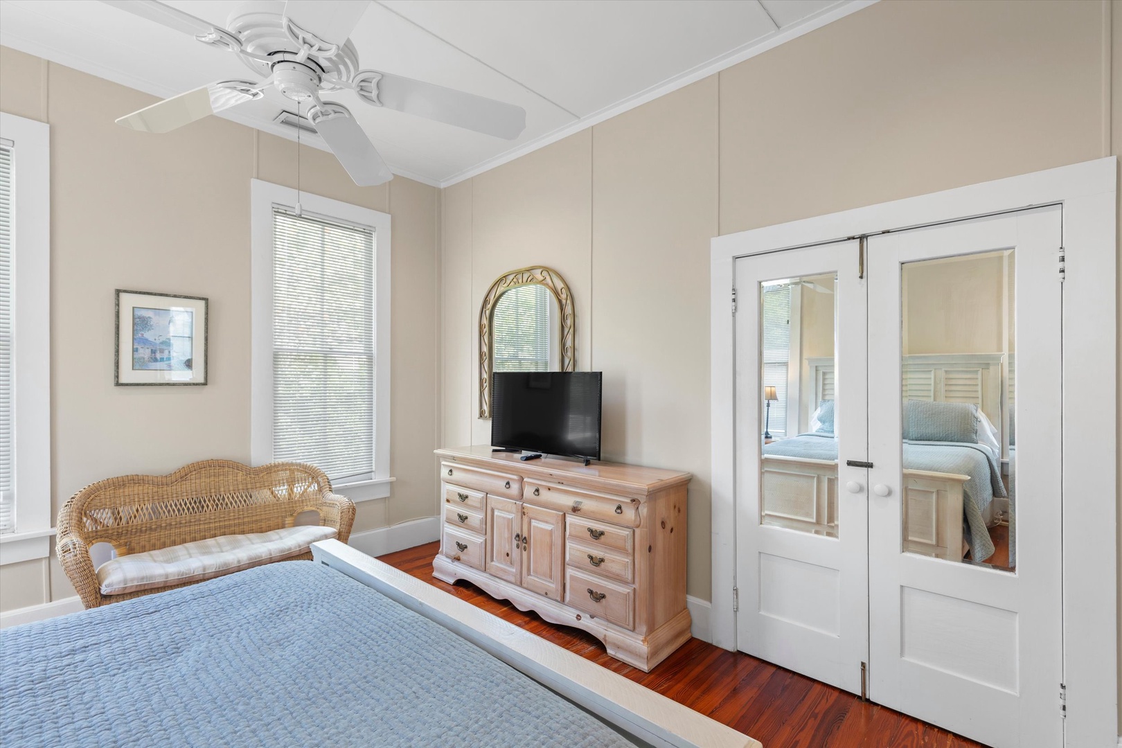 Rest easy in your serene bedroom with warm hardwood floors, a ceiling fan for comfort, and charming French doors opening to another cozy space—perfect for peaceful nights and refreshing mornings.