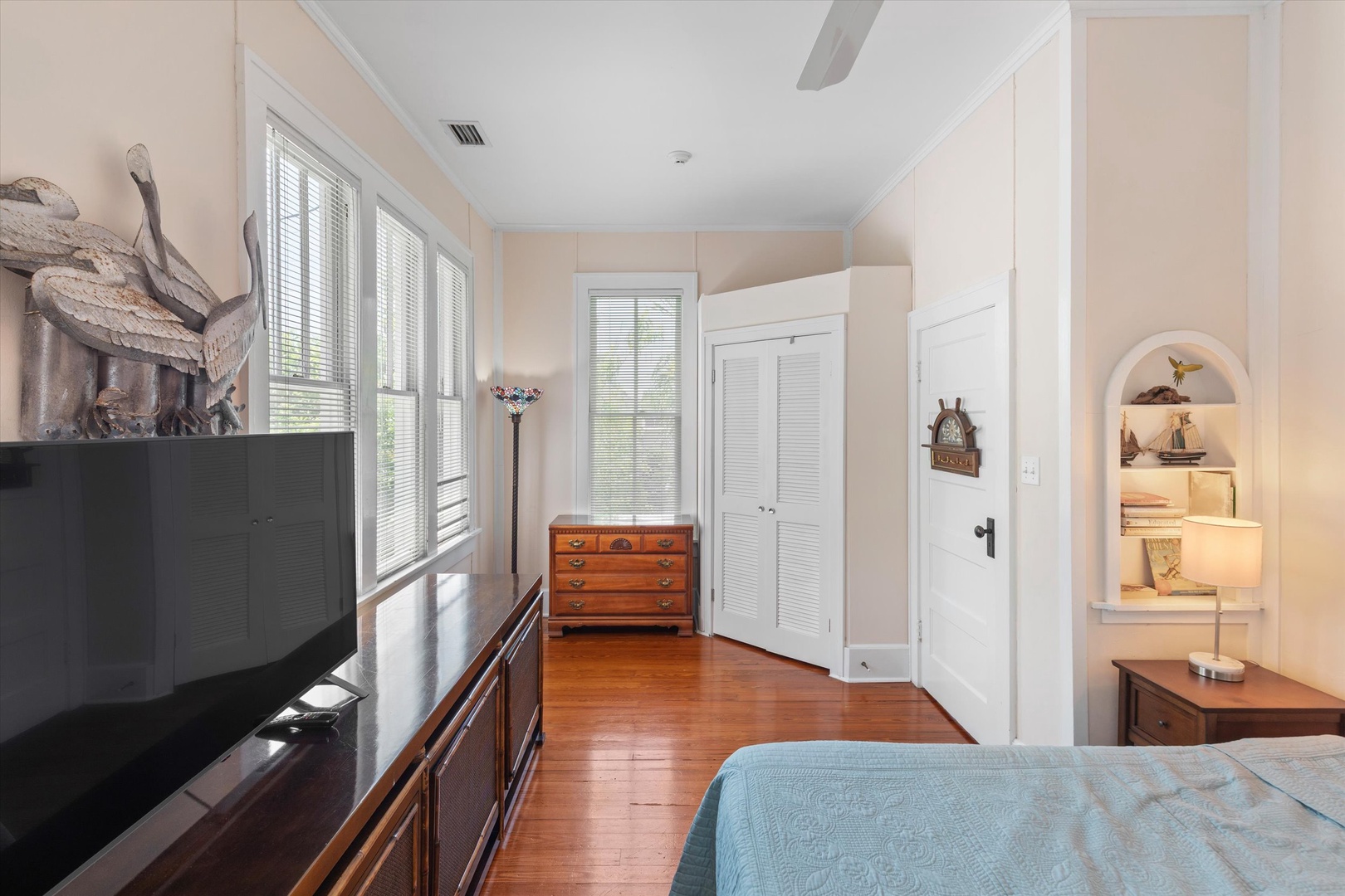 Unwind in this peaceful bedroom with warm hardwood floors, charming coastal décor, and soft natural light filtering through shuttered windows to create your ideal retreat.