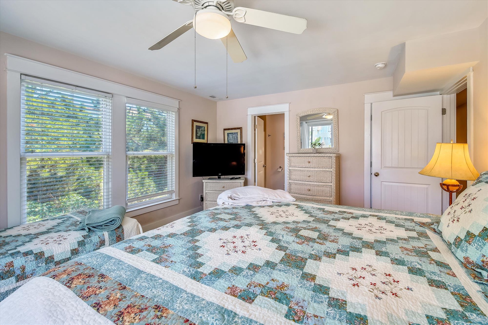 Drift off beneath the ceiling fan in this inviting bedroom, where soft linens and natural light through wide windows create your peaceful coastal retreat.