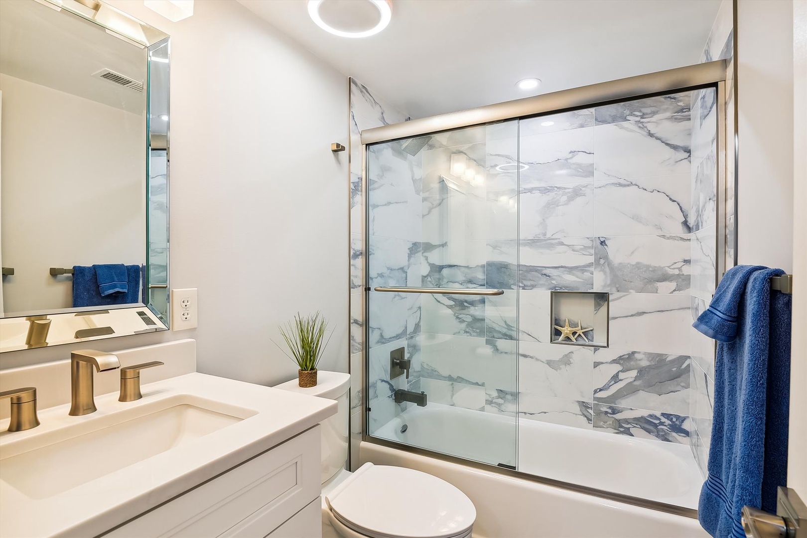 Unwind in your private spa-like bathroom, where marble-look tiles and gold fixtures create a serene coastal retreat. Plush towels and a soaking tub await your arrival.