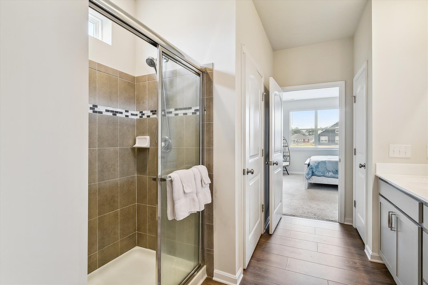Step into your private en-suite bathroom featuring a spacious walk-in shower with stylish tile work and plush towels. The bedroom awaits just beyond, offering a peaceful retreat.