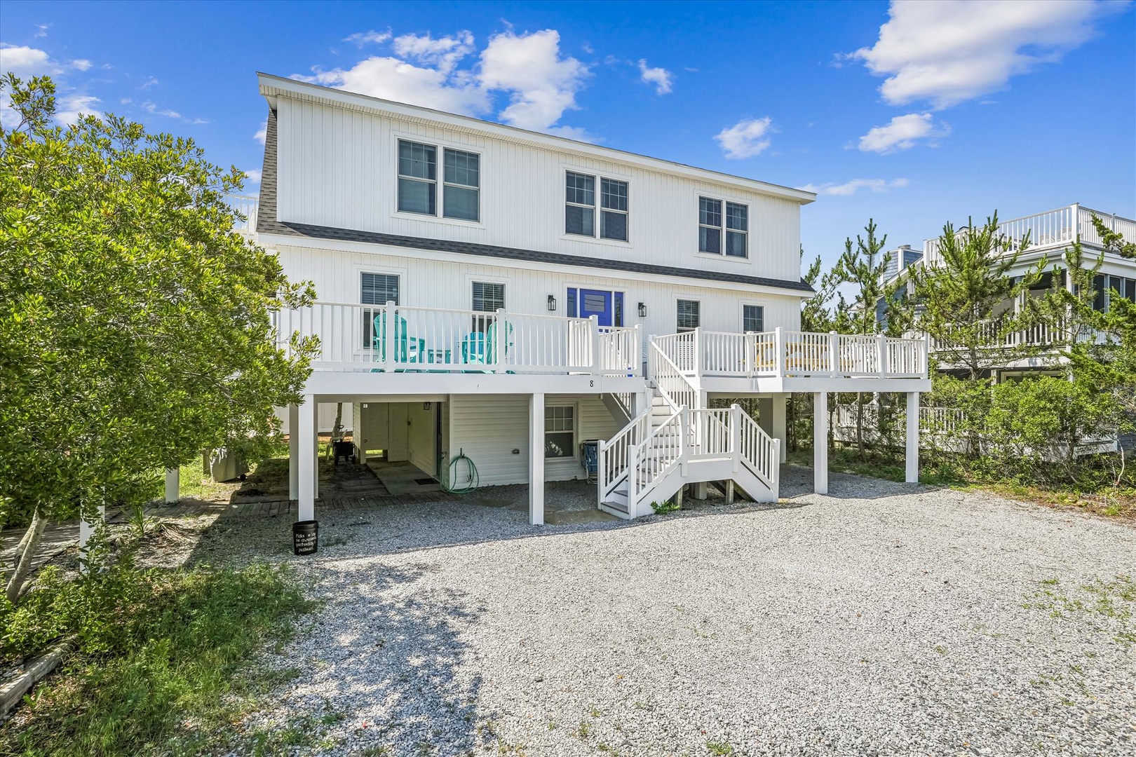 Charming coastal home with spacious deck and parking, surrounded by lush greenery under sunny skies.