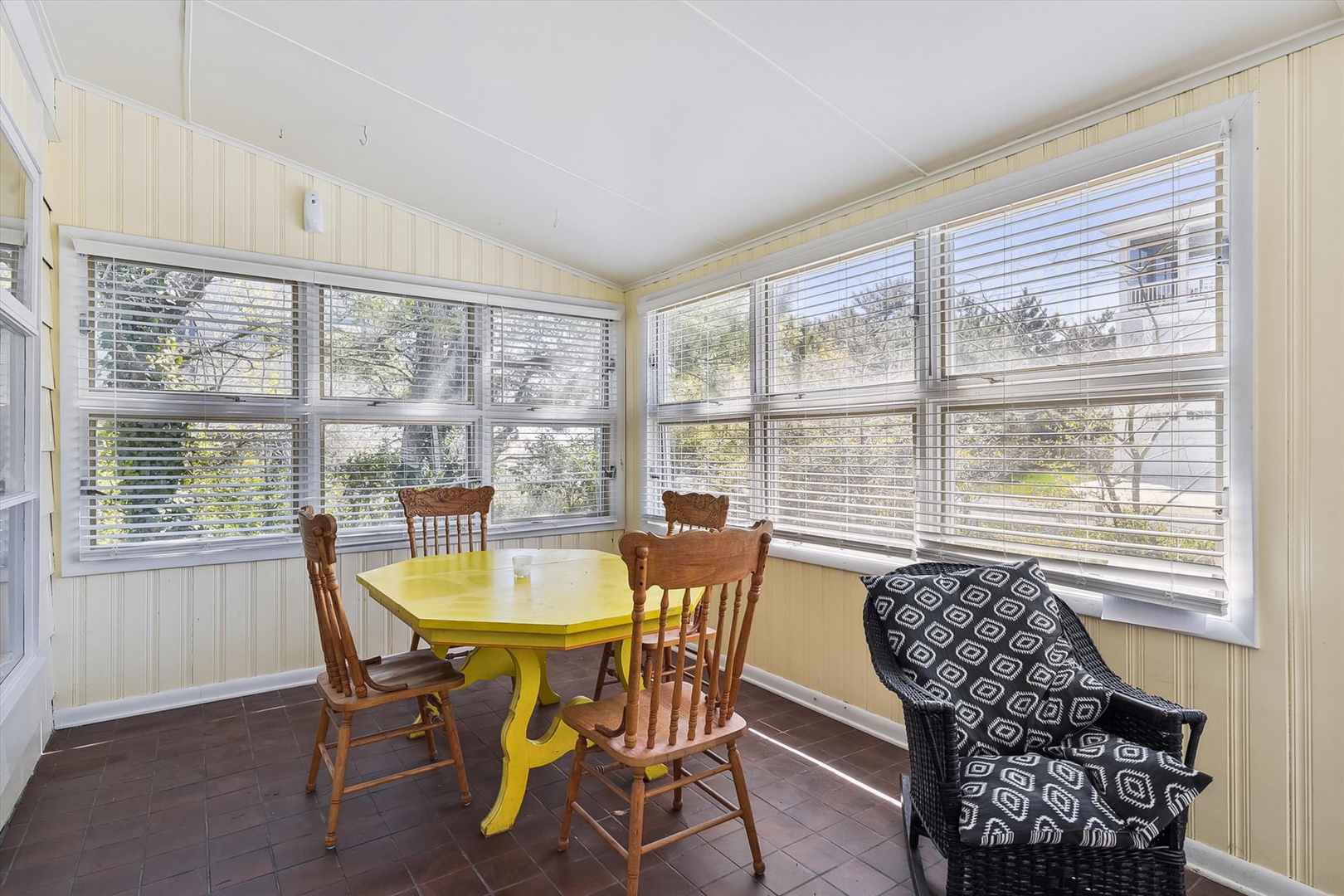 Enjoy your morning coffee in this bright sunroom with garden views, featuring a cheerful yellow table and cozy seating surrounded by natural light.
