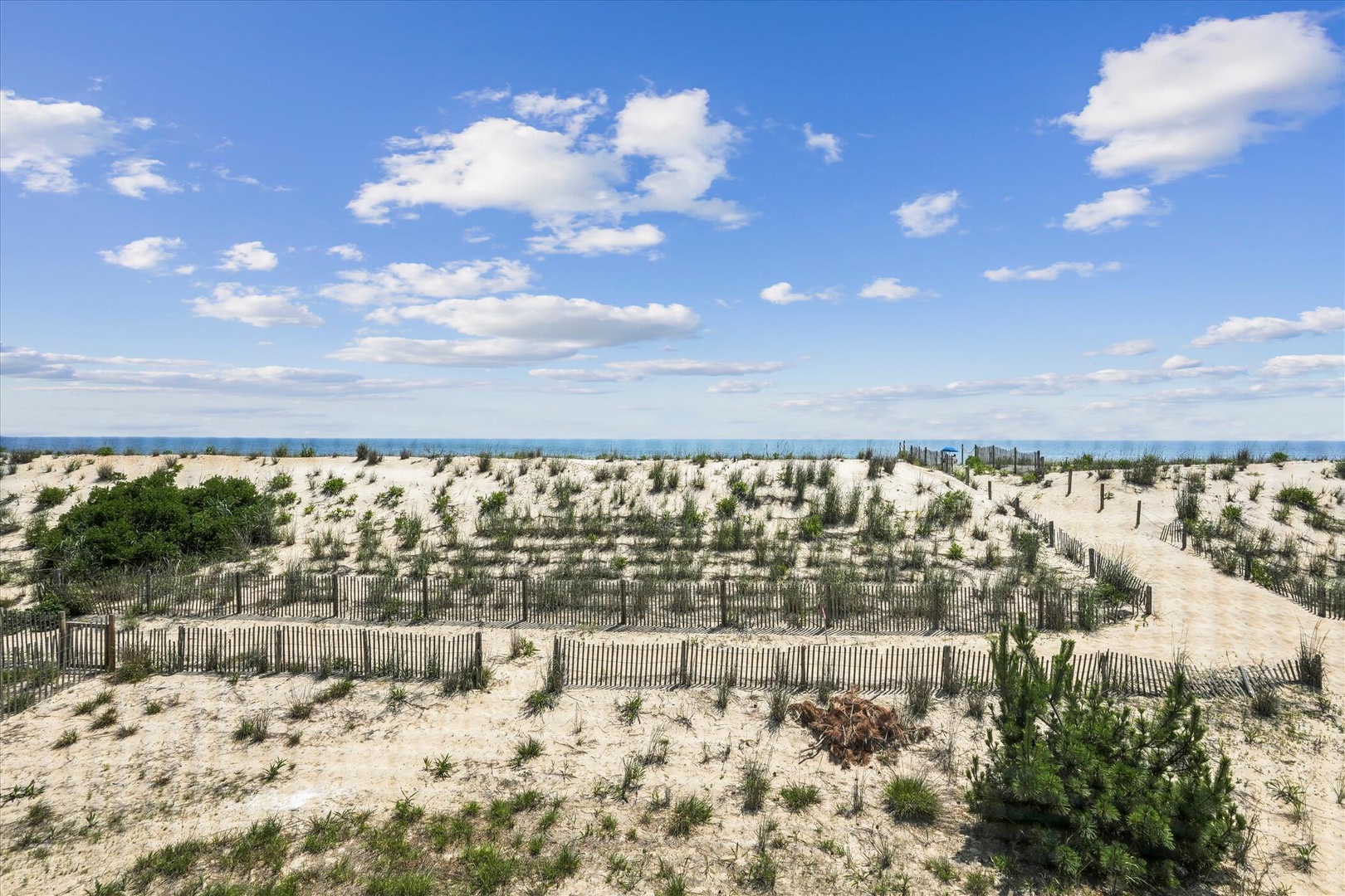Sandy dunes and sea grasses mark the preserved coastal landscape surrounding the property, offering a serene beachside setting under expansive blue skies.