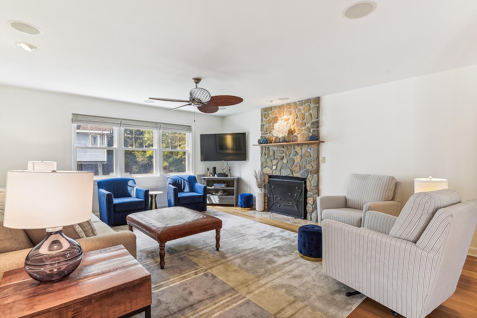 Gather around the handsome stone fireplace in this bright living room, where plush seating and warm wood floors invite you to unwind after a day exploring the area.