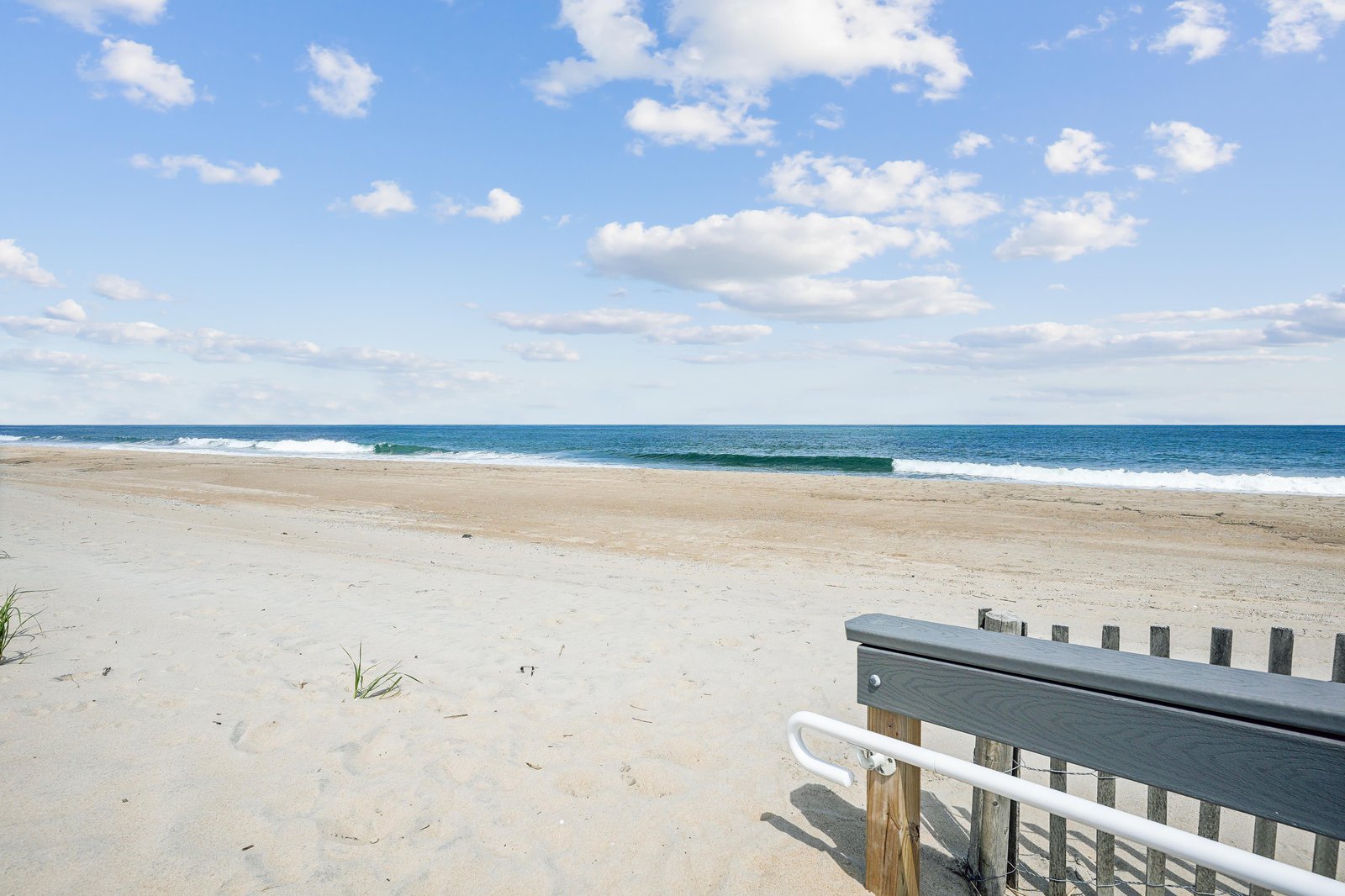 This pristine beach stretches along the property's surroundings, offering soft sands and calm blue waters beneath a peaceful sky dotted with fluffy clouds.