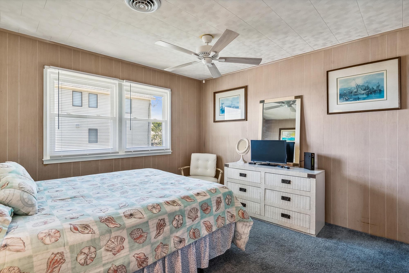 Unwind in this coastal-inspired bedroom where warm wood tones meet ocean hues. Your ceiling fan keeps you cool while you enjoy peaceful views and charming seaside artwork.