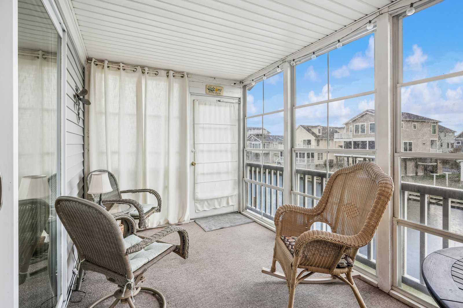Step onto your private screened-in porch, where wicker rockers invite you to sip morning coffee and watch the neighborhood come alive beneath bright coastal skies.