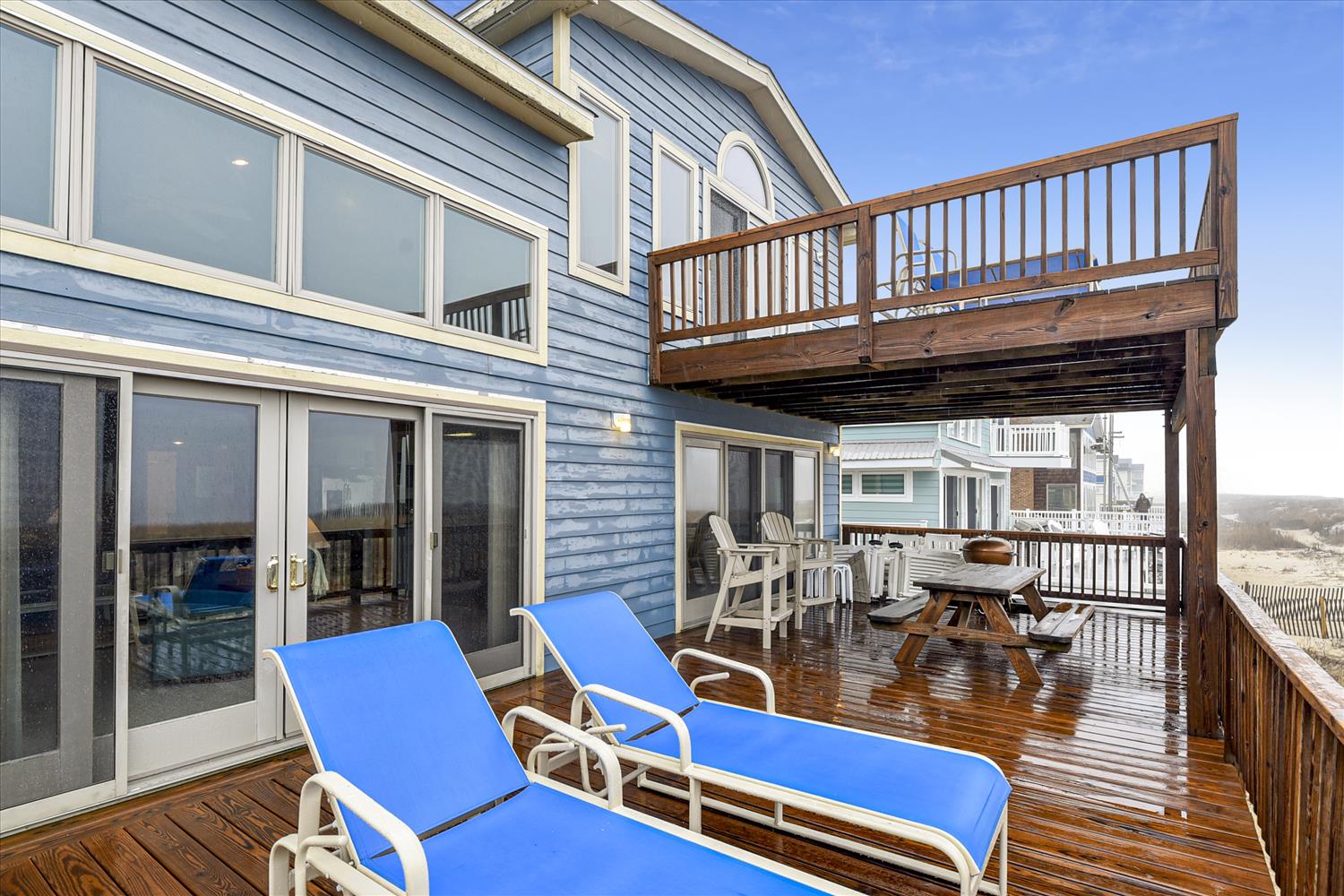 A spacious multi-level deck with ocean views stretches across the back of a charming blue coastal home, offering you plenty of room to lounge in the sun or enjoy meals together in the fresh air.