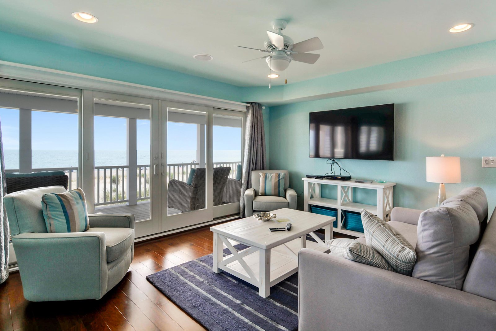 Step into your bright, coastal-inspired living room where turquoise walls meet stunning ocean views through floor-to-ceiling glass doors, inviting you to unwind in comfort and let the sea breeze refresh your spirit.