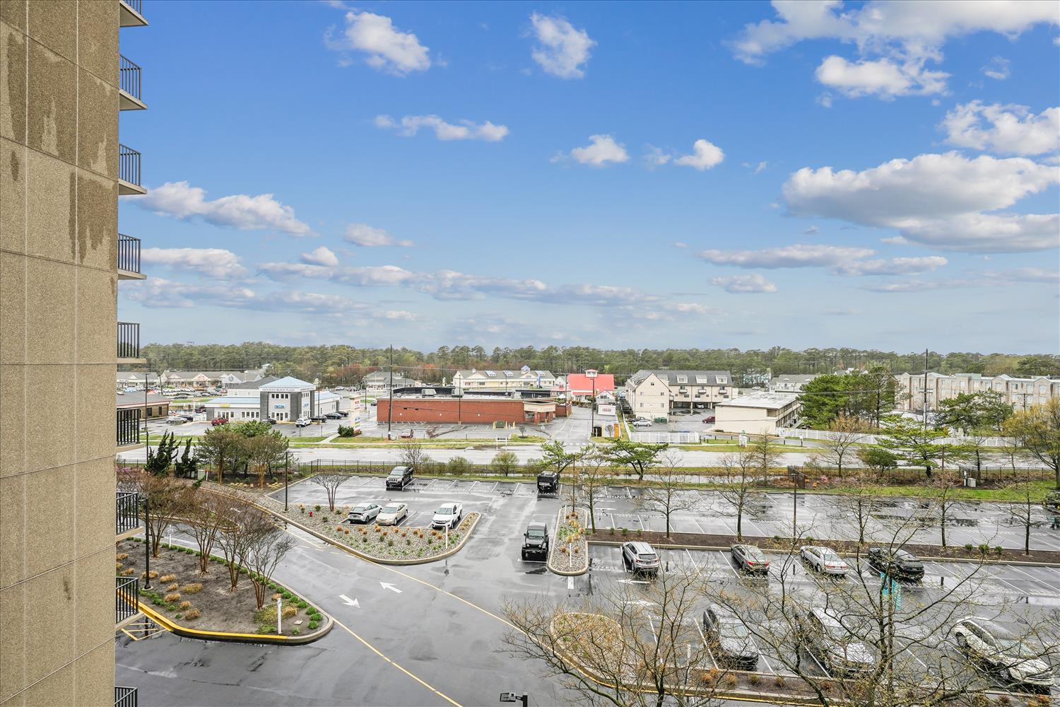 Daytime view overlooking the property entrance and surrounding neighborhood, with parking areas, commercial buildings, and tree-lined streets visible from the building.