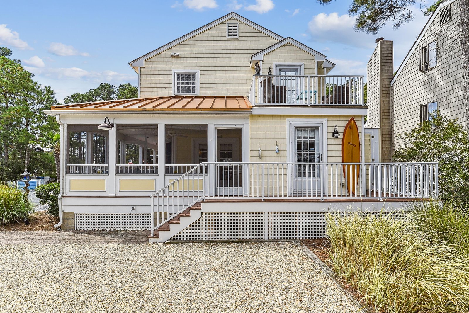 A charming coastal cottage with wraparound porches and a bright surfboard accent, set in a quiet neighborhood with natural landscaping and ample parking.