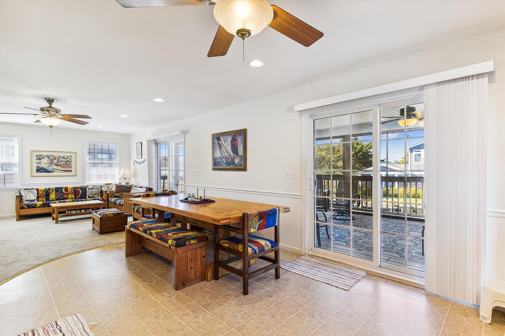 Settle into your bright, open living space where coastal charm meets comfort. Ceiling fans keep you cool as you gather at the wooden dining table, and sunlight streams through glass doors that open to your private deck outside.