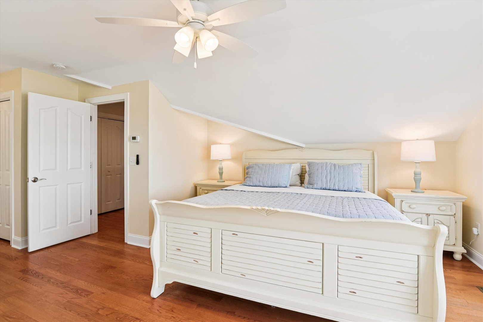 Wake up to soft morning light in your spacious bedroom, featuring a plush queen bed, gleaming hardwood floors, and a gentle ceiling fan overhead to keep you comfortable.